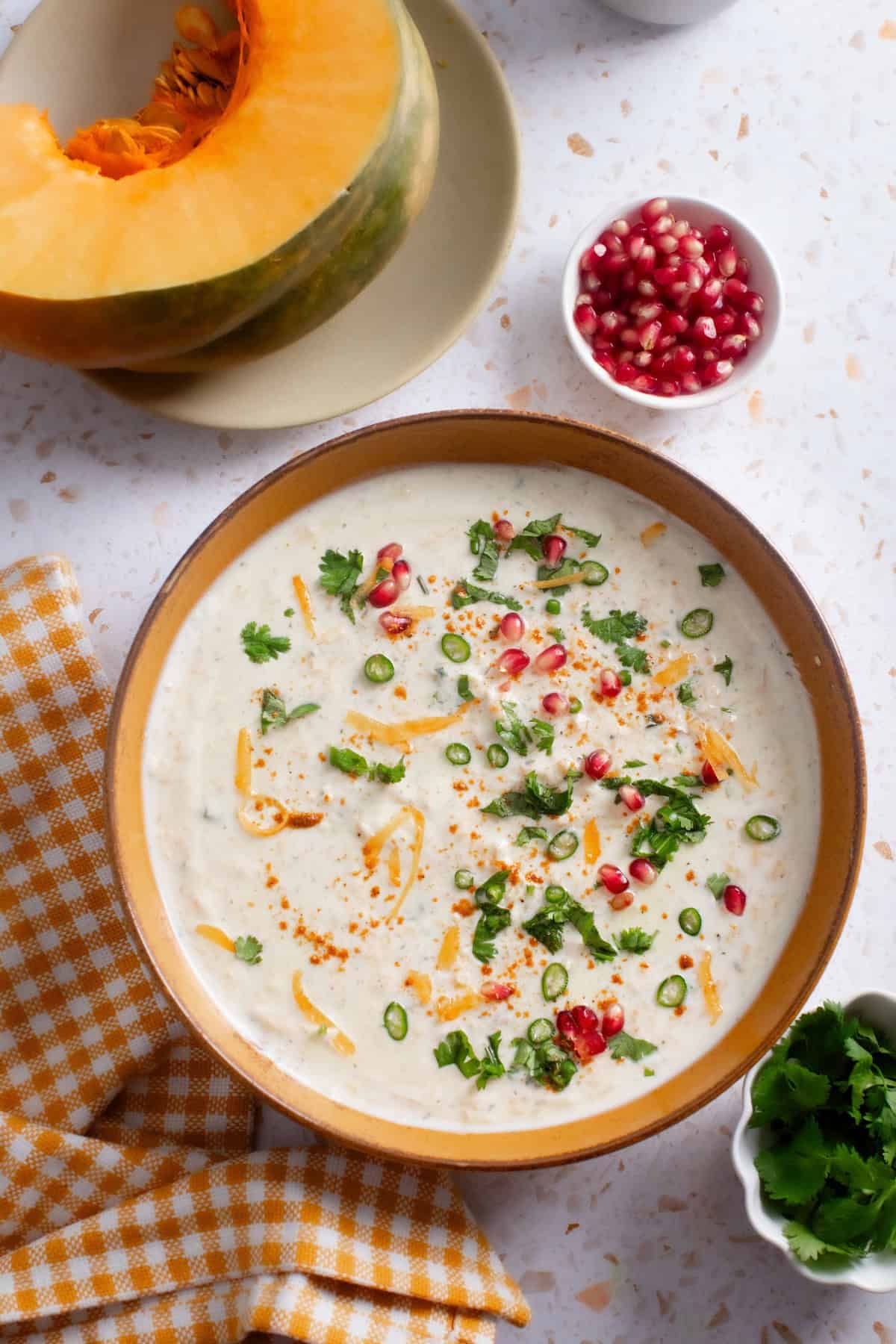 Pumpkin raita served in a mustard colored bowl with pomegranate and cilantro garnish.