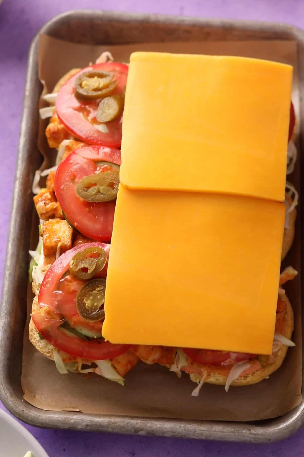 Slider buns are topped with cucumber, tomatoes, cheese slices and jalapenos.