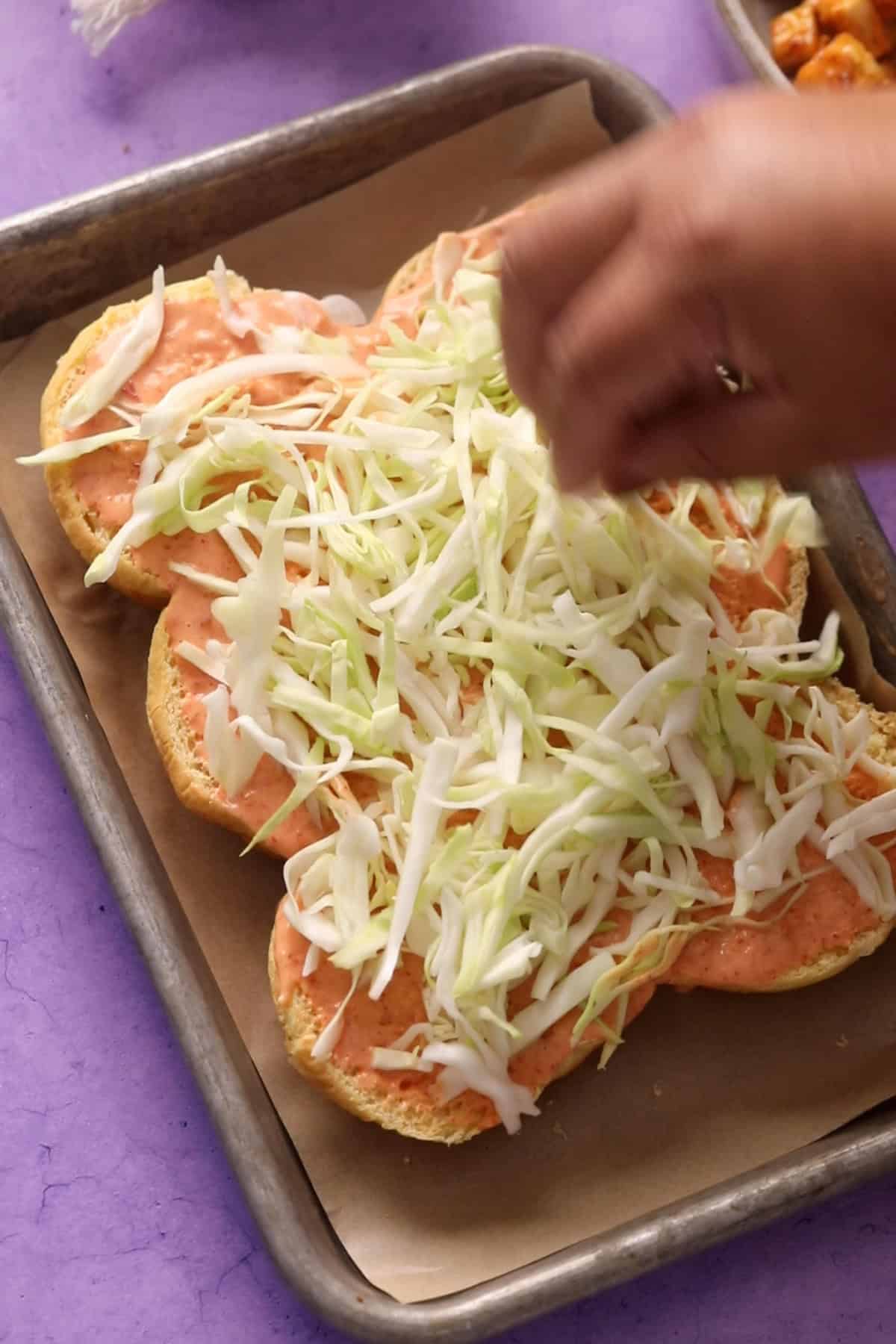 Sliced slider buns are spread with bang bang sauce and shredded cabbage. 