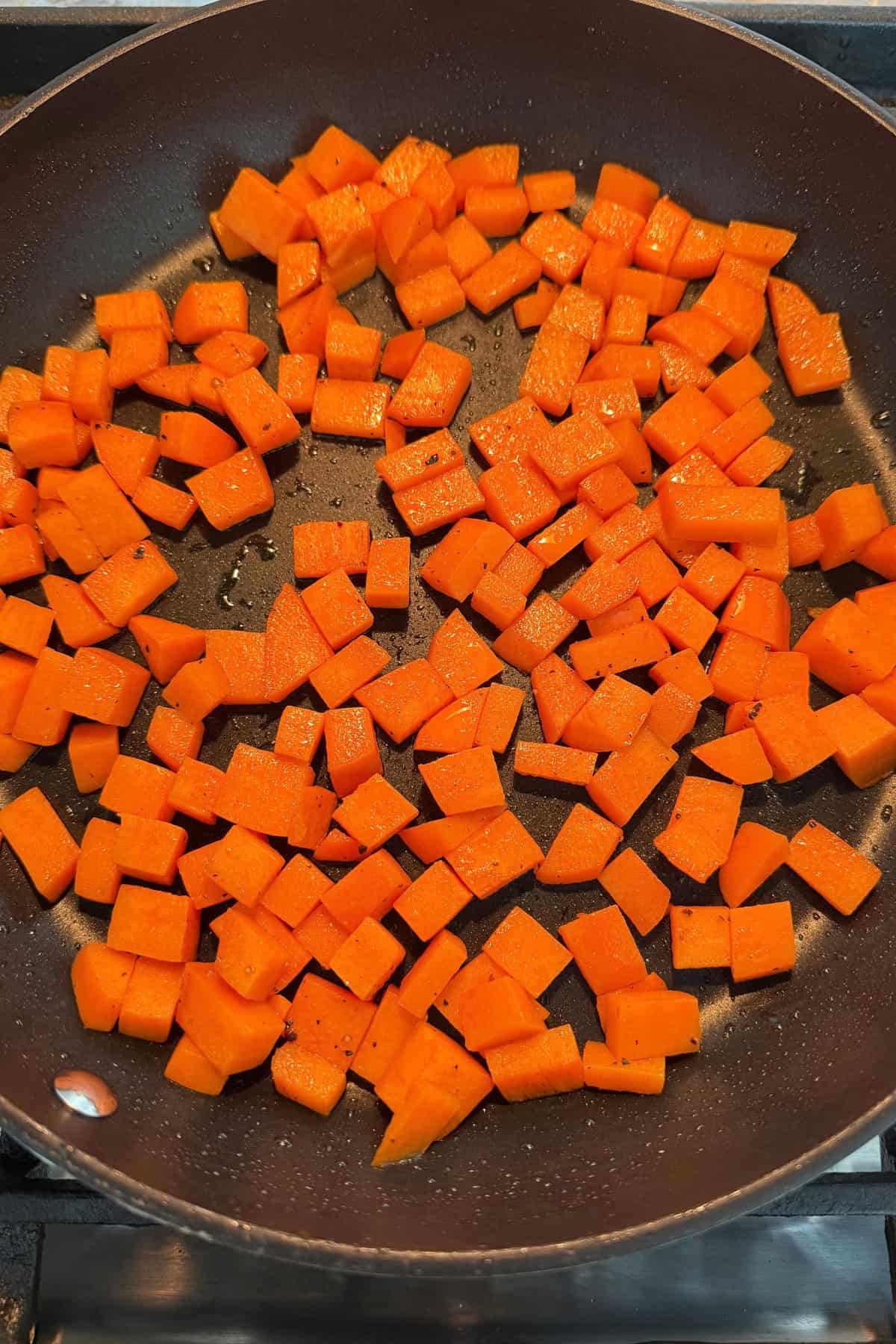 Pan fried diced sweet potato in a black pan.