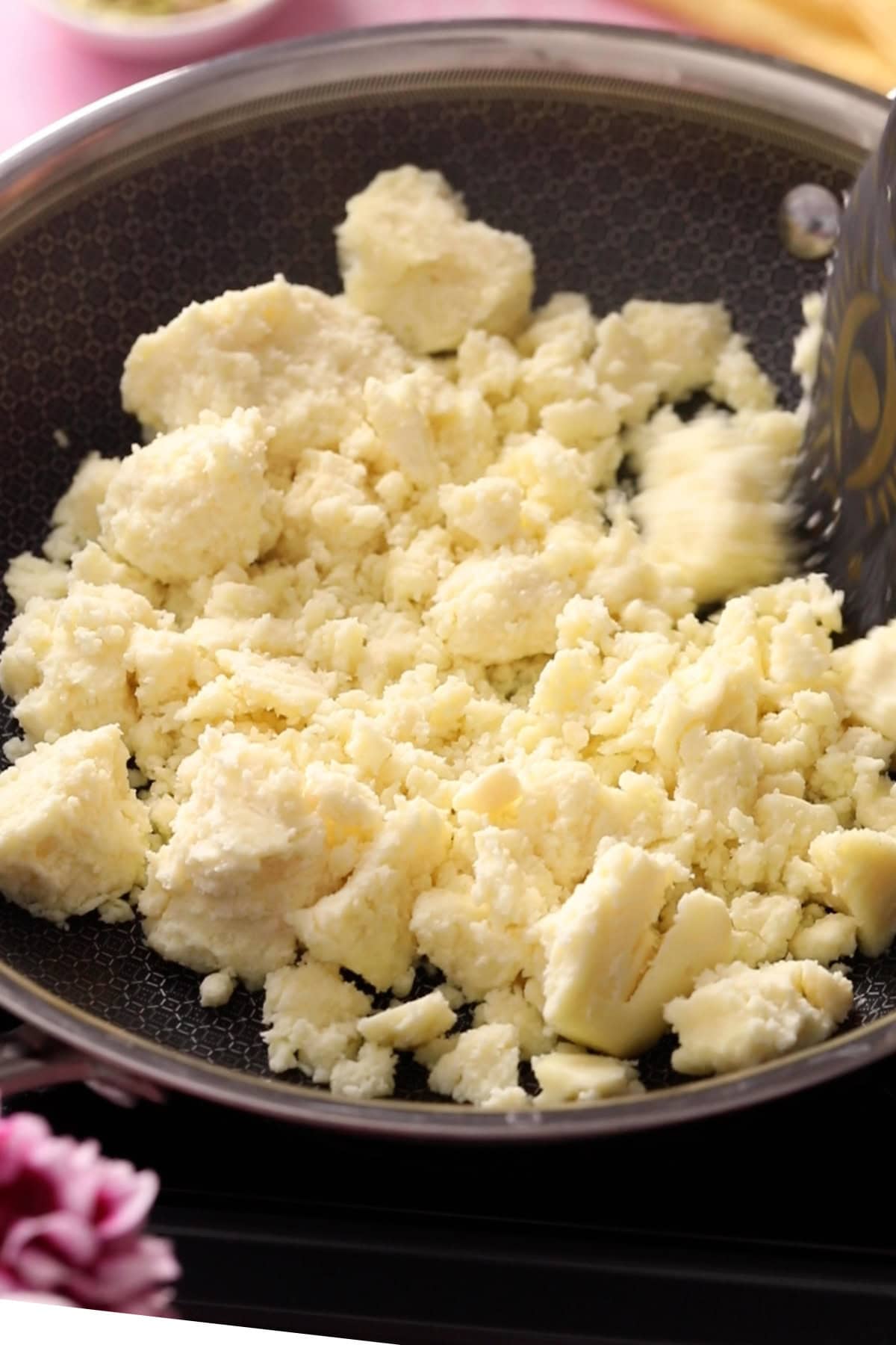 Crumbled khoya in a large black skillet.