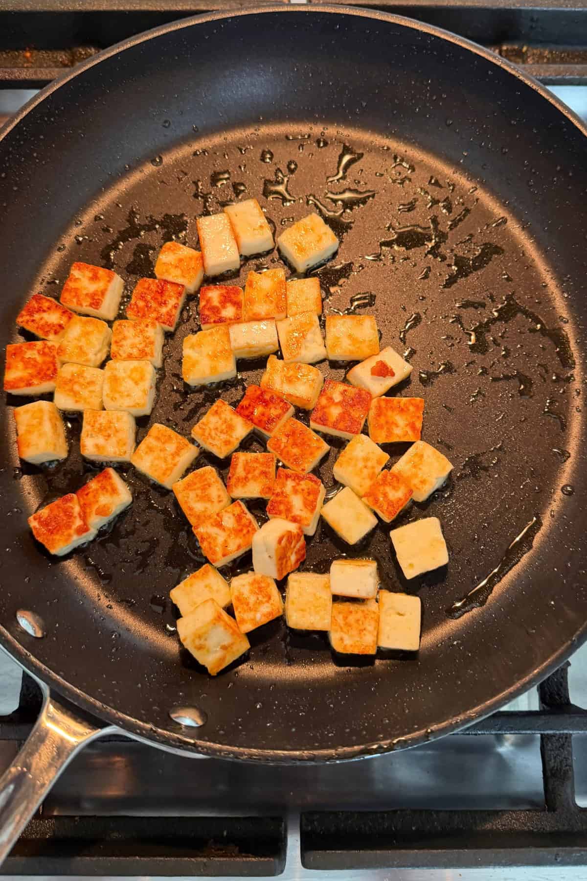 Pan fried diced paneer in a black pan.