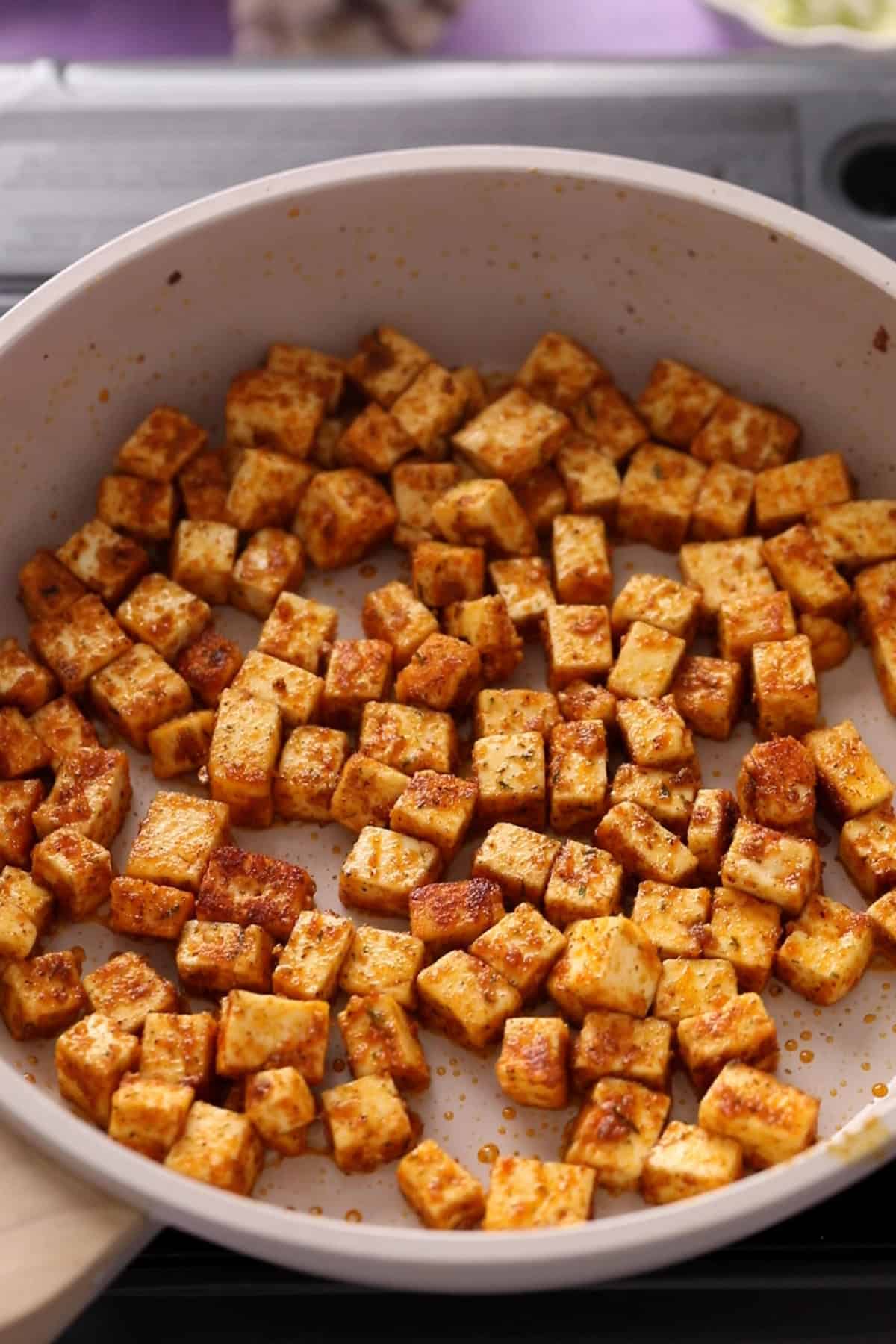 Cubed paneer browning in a light-colored frying pan